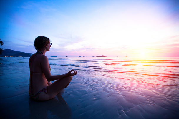 молодая женщина практикует йогу на пляже на закате - Фото, изображение