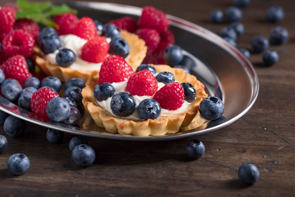  Dessert tarts with raspberries and blueberries on a wooden table. Closeup of fancy gourmet fresh berry dessert tarts. - Photo, Image