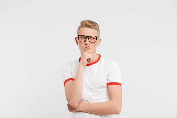 Image of concentrated guy in eyeglasses looking aside with brooding gaze and touching chin isolated over white background - Fotó, kép