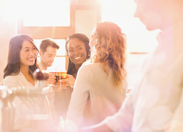 Women friends toasting beer glasses in sunny bar - Photo, Image