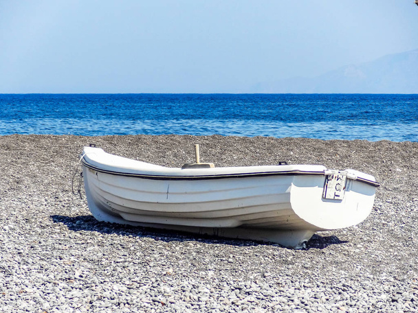 Lonely rowing boat on the pebbled beach of Santorini Greece - Photo, Image