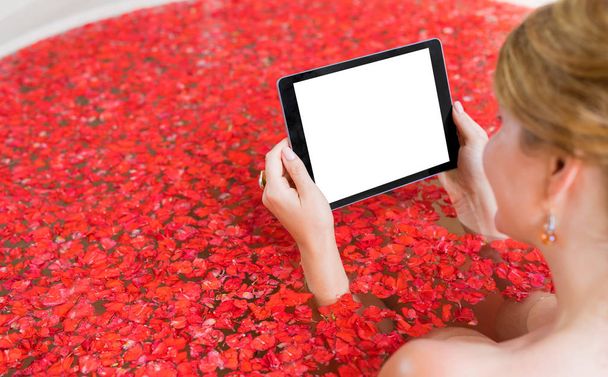 Frau benutzt Tablette in rotem Blütenbad - Foto, Bild