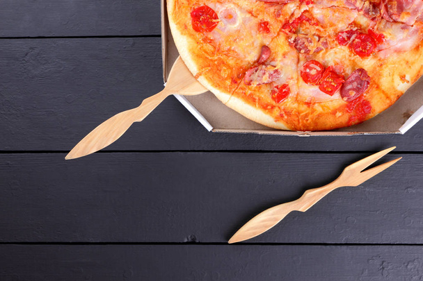 Pizza su fondo nero in legno con posate in legno, pizza italiana con pomodori, salsicce e formaggi, fast food, cibo festivo su fondo scuro, spazio fotocopie, cucina italiana, arte
 - Foto, immagini