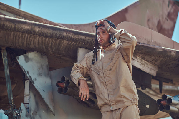 Mechanic in uniform and flying helmet standing near an old war fighter-interceptor in an open-air museum. - Photo, Image