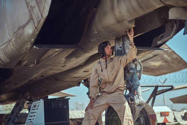 Mechaniker in Uniform und Flughelm, führt Wartung eines Kampfflugzeugs in einem Freilichtmuseum durch. - Foto, Bild
