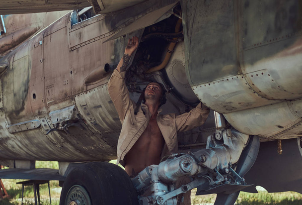 Mecánico en uniforme y casco de vuelo lleva a cabo el mantenimiento de un viejo bombardero militar en el museo al aire libre
. - Foto, Imagen