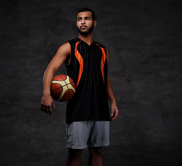 Portret afro-amerykański sportowiec. Koszykarz w sportowej z piłką na ciemnym tle. - Zdjęcie, obraz