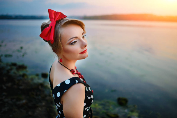 Krásná mladá žena oblečená, stojící u jezera, na pozadí západ slunce. - Fotografie, Obrázek