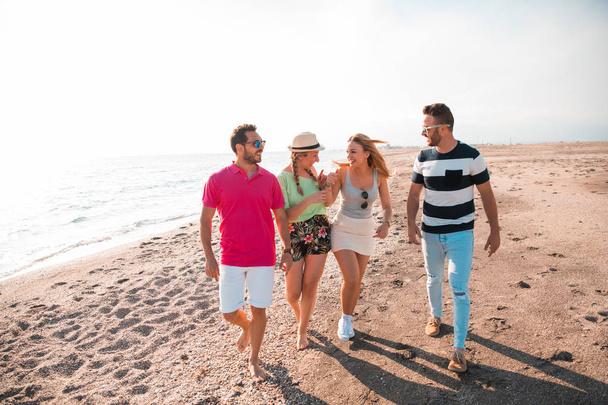 幸せな若い人たちのグループは、美しい夏の夕日のビーチで歩く。友達と休日のコンセプト - 写真・画像
