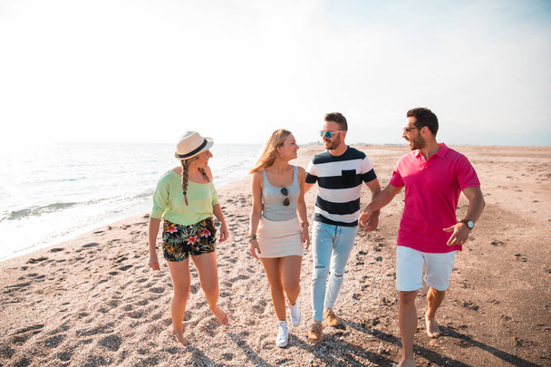 Grupa szczęśliwych młodych ludzi spacerujących po plaży w piękny letni zachód słońca. Przyjaciele i koncepcja wakacji - Zdjęcie, obraz