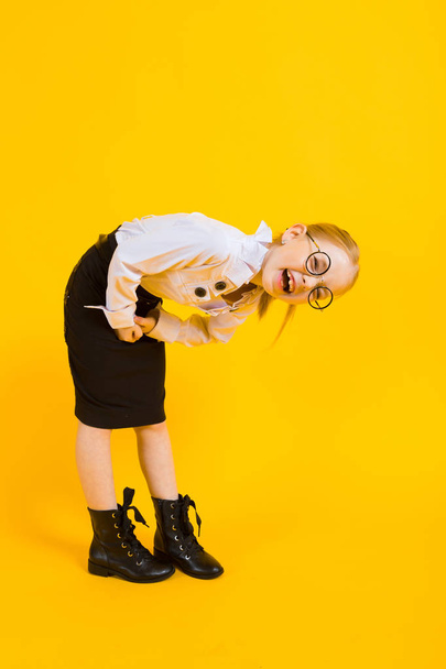 Chica con el pelo rojo sobre un fondo amarillo. Una encantadora chica con gafas transparentes sostiene sus manos contra su estómago
. - Foto, Imagen