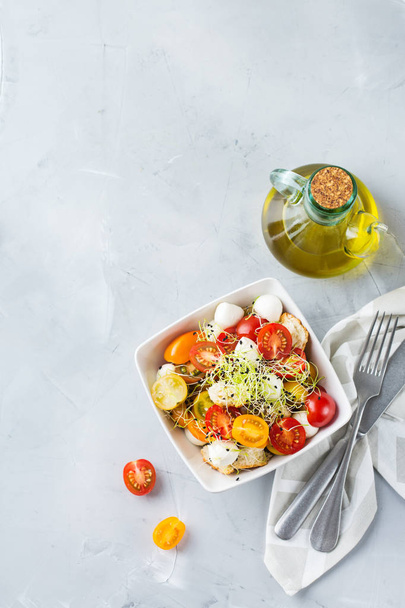 Food and drink, healthy eating concept. Salad with assortment of organic cherry tomatoes, mozzarella cheese, toasted bread and microgreen on a kitchen table. Top view flat lay background - Photo, Image