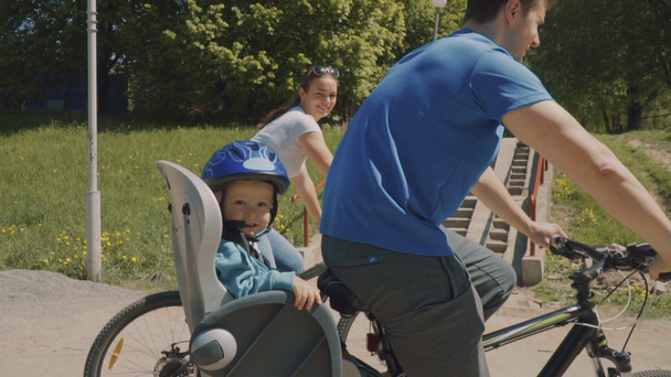 Jovem mais longe com seu filho pequeno estão montando uma bicicleta no parque. Movimento lento
 - Filmagem, Vídeo