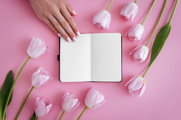 Manicure. Opened noteboog around beautiful flowers. Pink background. Flat lay style. - Foto, afbeelding