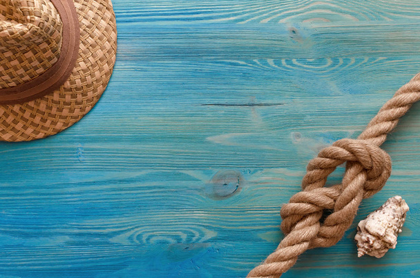Summer vacation background with copy space. Tourist hat, rope knot and seashell on blue wooden table background. - Foto, afbeelding