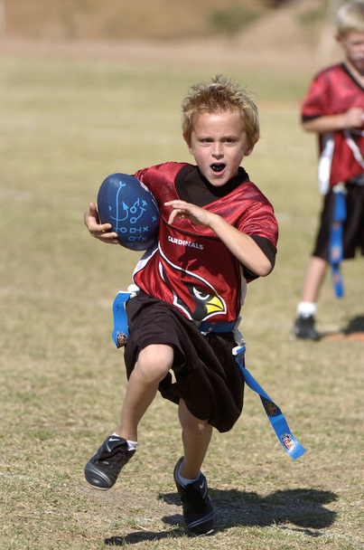 Flaggenfußballspiel, das von Kindern mit Action und Spaß gespielt wird. Flag Football ist eine Version des American Football, wo die grundlegenden Spielregeln dem Tackling Football ähneln, aber statt Spieler auf den Boden zu hauen, wird eine Fahne mitgenommen. - Foto, Bild