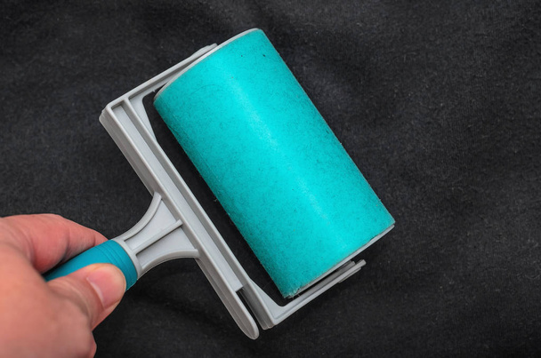 Using the sticky lint roller on a black fabric to remove dust, fur, hair of the shirt. Cleaning a fabric with a washable blue sticky roller. - Photo, Image