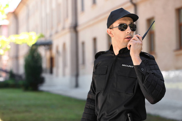 Male security guard using portable radio transmitter outdoors - 写真・画像