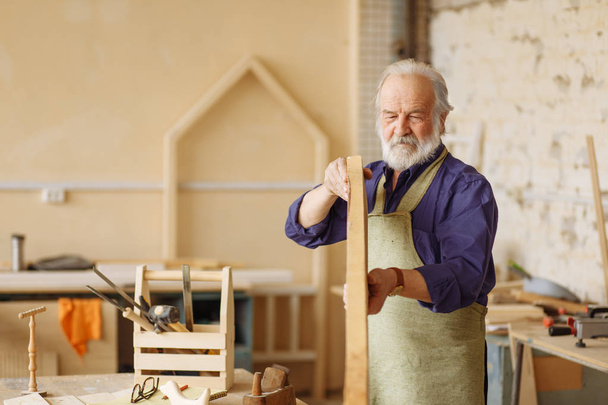 old craftsman with grey hair, moustache and beard moving planks - Foto, afbeelding