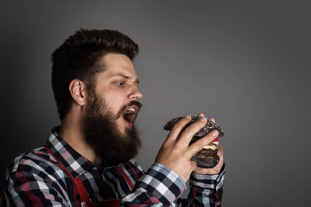 junger Mann beißt auf frischen leckeren schwarzen Hamburger - Foto, Bild