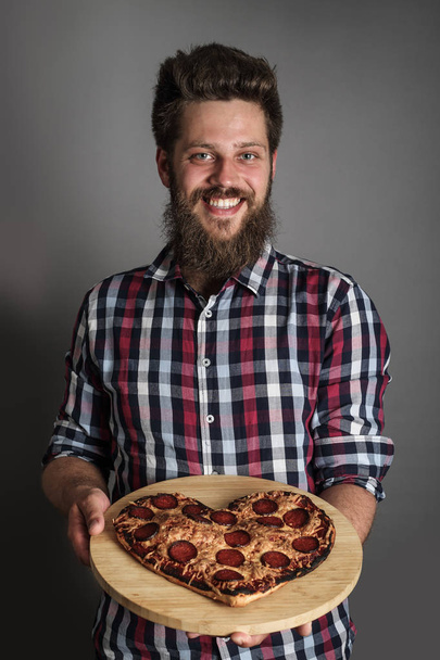 Happy smiling man gives burned heart shapes pizza - Fotó, kép