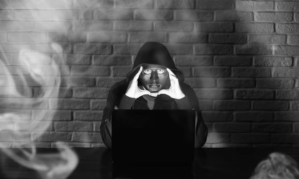 Хакер в черной маске и капюшоне за столом
 - Фото, изображение