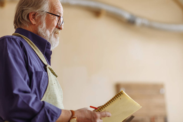 close-up side view cropped portrait of old carpenter with notepad - Фото, изображение