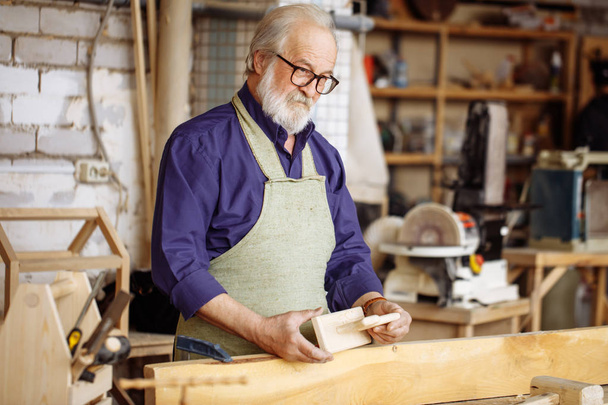 thoughtful old man holding wooden dog and looking at it in the repair shop - Foto, immagini