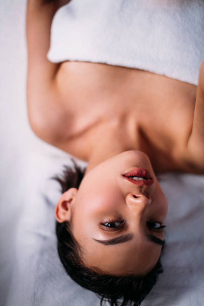 good-looking asian girl is lying on the bed and looking at the c - Zdjęcie, obraz
