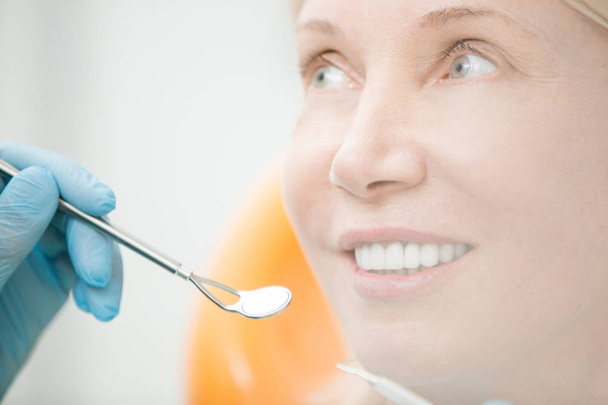 Healthy mature woman with toothy smile looking at dentist with mirror before check-up - Photo, Image