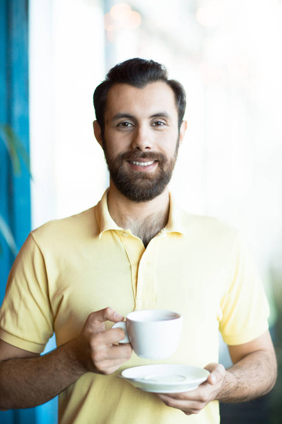 Jeune manager avec une tasse de café vous regardant avec le sourire l'un des jours ouvrables
 - Photo, image