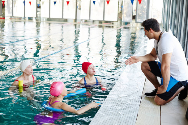 Kolme vanhempi uimarit vedessä puhuvat nuorten kouluttaja suosituksia ennen uimista
 - Valokuva, kuva