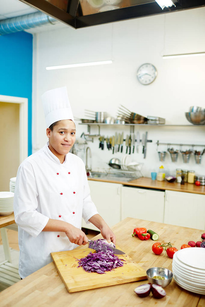 Young successful professional in chef uniform cutting fresh purple cabbage for salad, soup or stew - Photo, Image