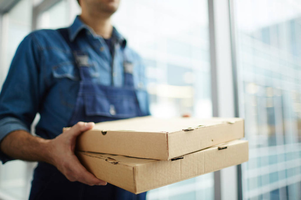 Two boxes with fast food being carried by delivery man in uniform for one of clients - Photo, Image