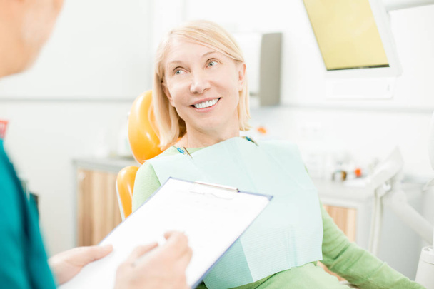 Glimlachend patiënt luisteren naar de aanbevelingen van haar tandarts na Pakketbronnen of genezing van tanden - Foto, afbeelding