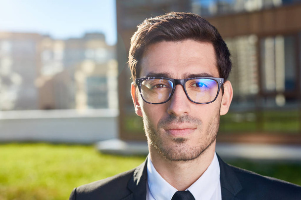 Young businessman in eyeglasses and formalwear looking at camera in urban environment - Photo, Image