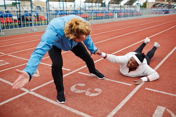 Young exhausted plus-sized woman in activewear talking to trainer pulling her towards finish line - Photo, Image