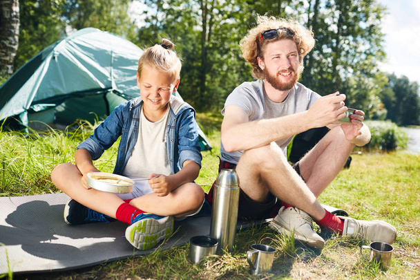 Dvě mladé výletníci sedí na zemi v přirozeném prostředí a po snídani v dopoledních hodinách - Fotografie, Obrázek