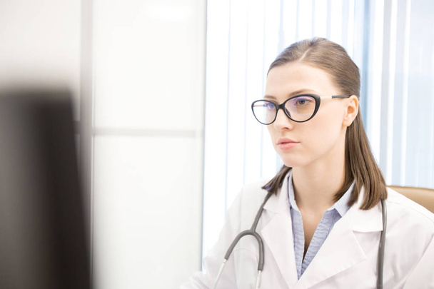 Nuori naislääkäri valkotakissa ja silmälaseissa konsultoi potilaita verkossa nykyaikaisilla klinikoilla
 - Valokuva, kuva