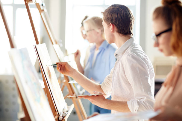 Kreativní člověk při pohledu na obrázek na stojan učitele při malování na lekce ve studiu umění - Fotografie, Obrázek
