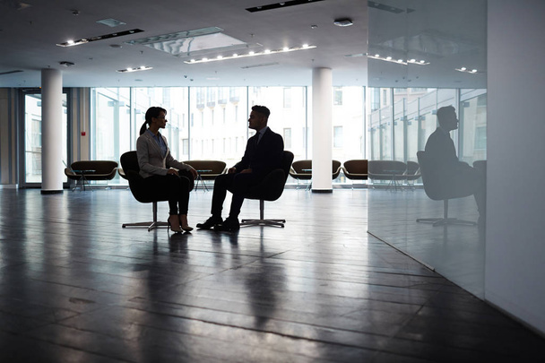 Jistý mladý manažer sedí naproti jejího mužského partnera při brainstormingu na společném projektu, vnitřní prostorné dim kanceláři lobby na pozadí - Fotografie, Obrázek
