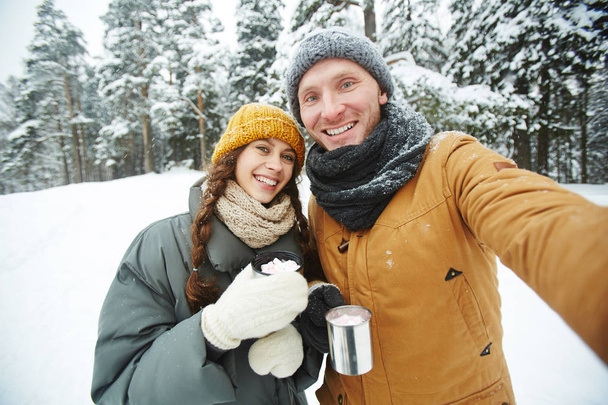 Joyeux jeunes dates en vêtements d'hiver faisant selfie dans la forêt d'hiver
 - Photo, image