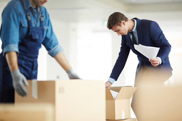 Сучасний бізнесмен у костюмі шукає необхідні документи в одній з коробок одразу після переїзду в новий офіс
 - Фото, зображення