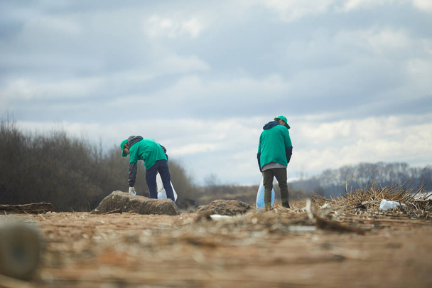 Twee actieve greenpeacers bezig met strooisel verlaten grondgebied ergens in de rand - Foto, afbeelding