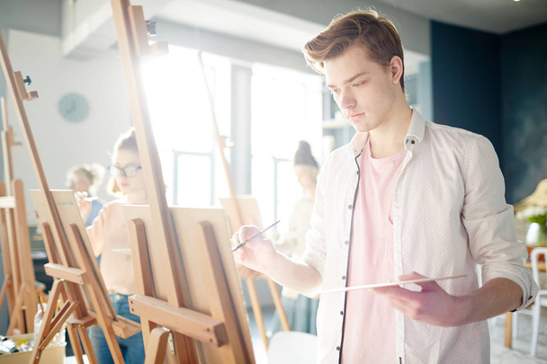Poważny facet z palety i farby, koncentrując się na malowanie na sztalugach w studio sztuki - Zdjęcie, obraz