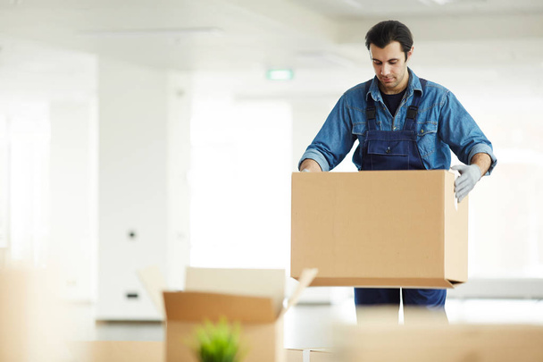 Trabajador de servicio de entrega joven que lleva cajas de cartón embaladas a una nueva oficina en un centro de negocios contemporáneo
 - Foto, imagen