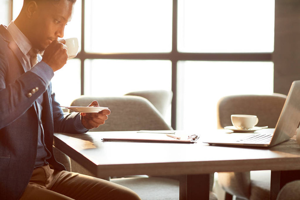 Молодий бізнесмен п'є чай і читає документ або думає про майбутню угоду з партнерами
 - Фото, зображення