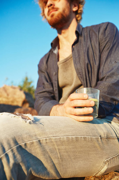 Nuori mies casualwear tilalla lasi virkistävää juomaa rentoutuen ulkona
 - Valokuva, kuva