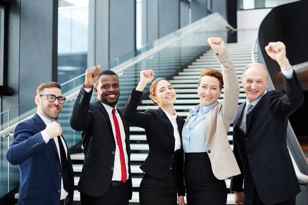 Reihe aufgeregter Mitarbeiter, die mit erhobenen Händen und zahmem Lächeln in die Kamera blicken, während sie den Erfolg feiern - Foto, Bild
