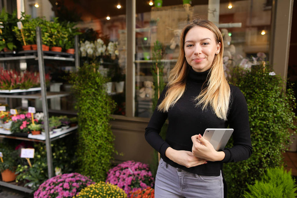 Жіночий кавказький менеджер квіткового магазину, що стоїть з планшетом біля кімнатних рослин
. - Фото, зображення